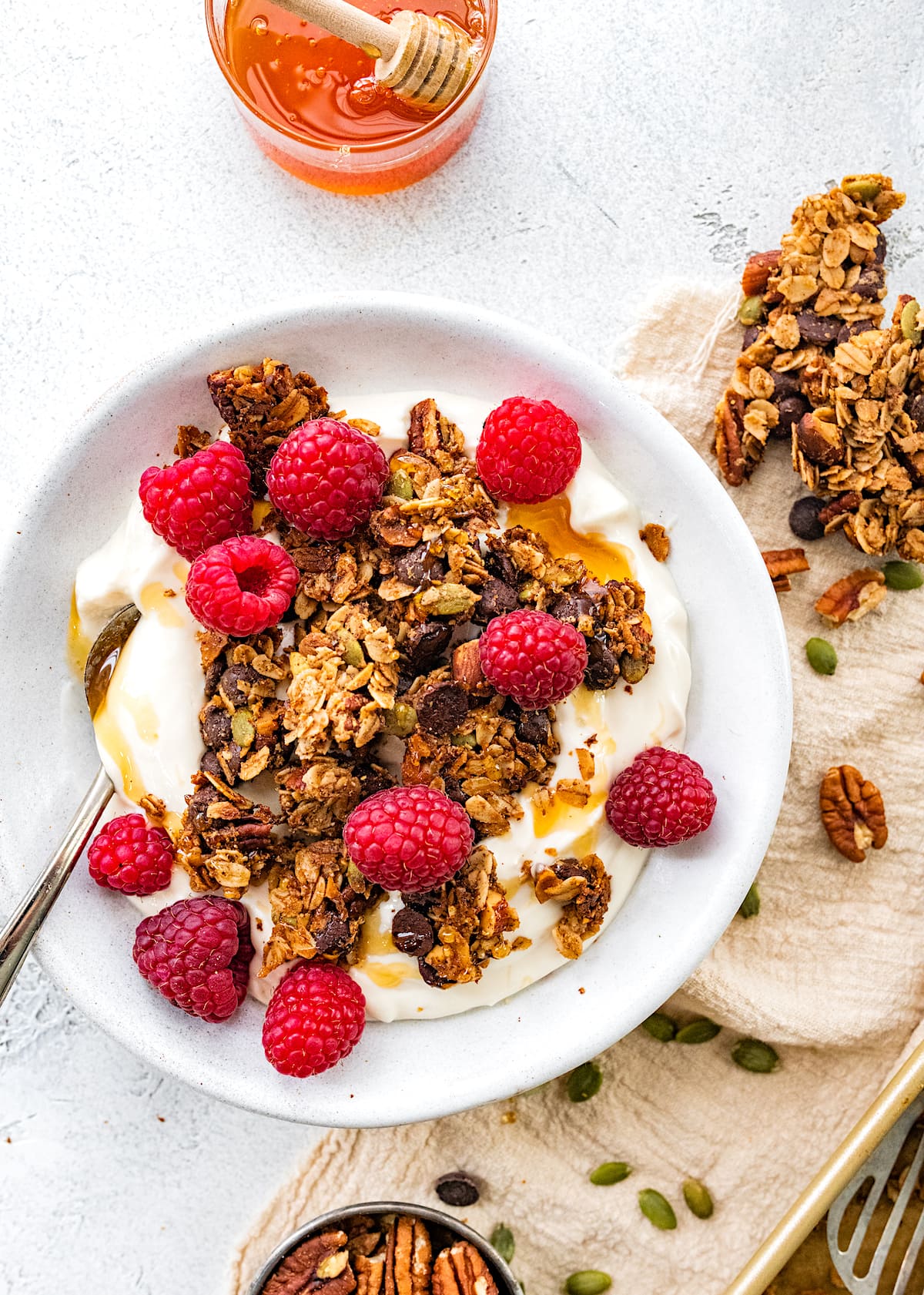 bowl of yogurt with chocolate chip cookie granola clusters, raspberries, a drizzle of honey, and spoon. 