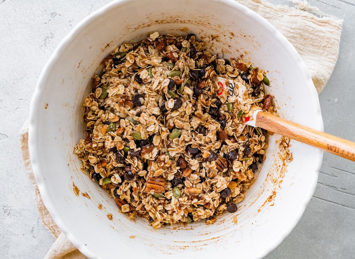 mixing chocolate chip cookie granola clusters in bowl with spatula. 