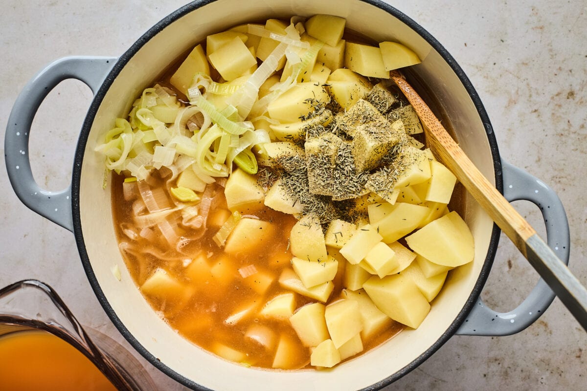 potato leek soup ingredients in large pot with wooden spoon. 