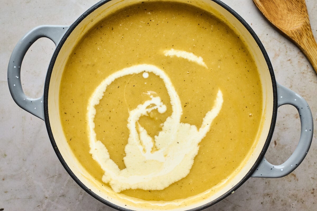 potato leek soup in large pot with drizzle of heavy cream.