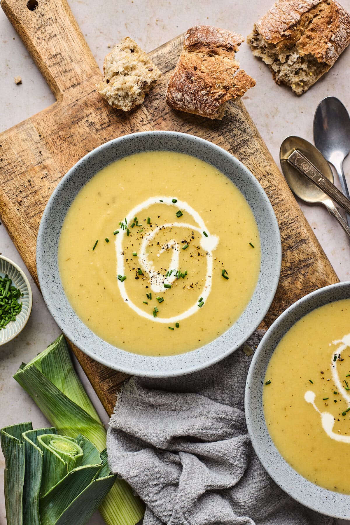 potato leek soup in bowl with drizzle of cream and herbs on wood board with crusty bread. 