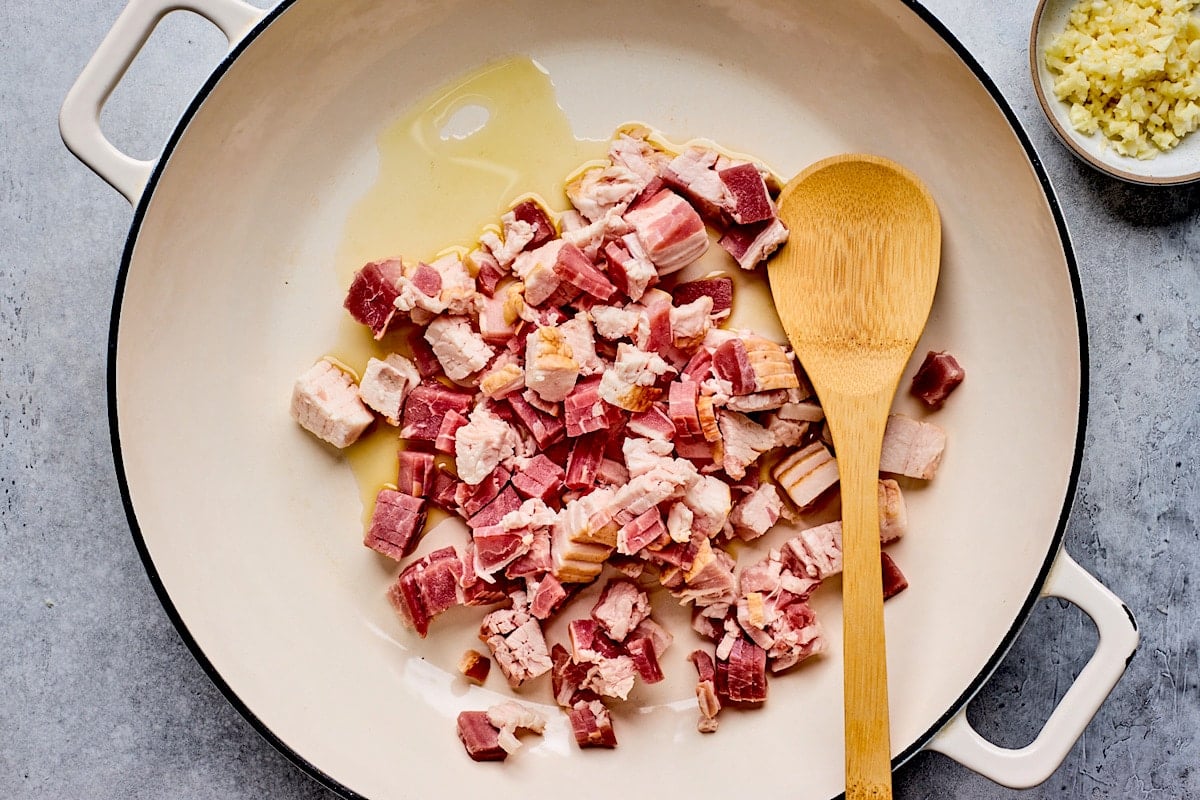 olive oil and chopped bacon in skillet with wooden spoon. 