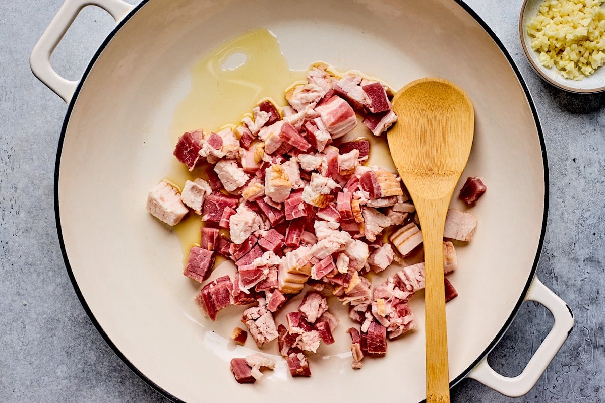 olive oil and chopped bacon in skillet with wooden spoon.