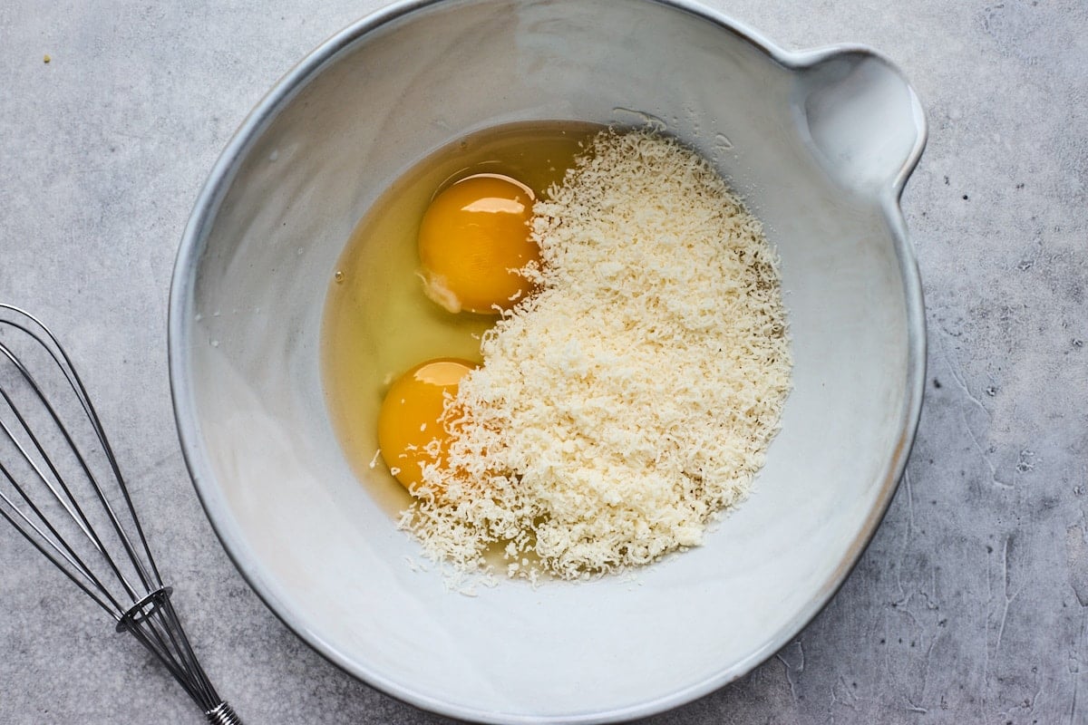 Parmesan cheese and eggs in mixing. bowl with whisk.