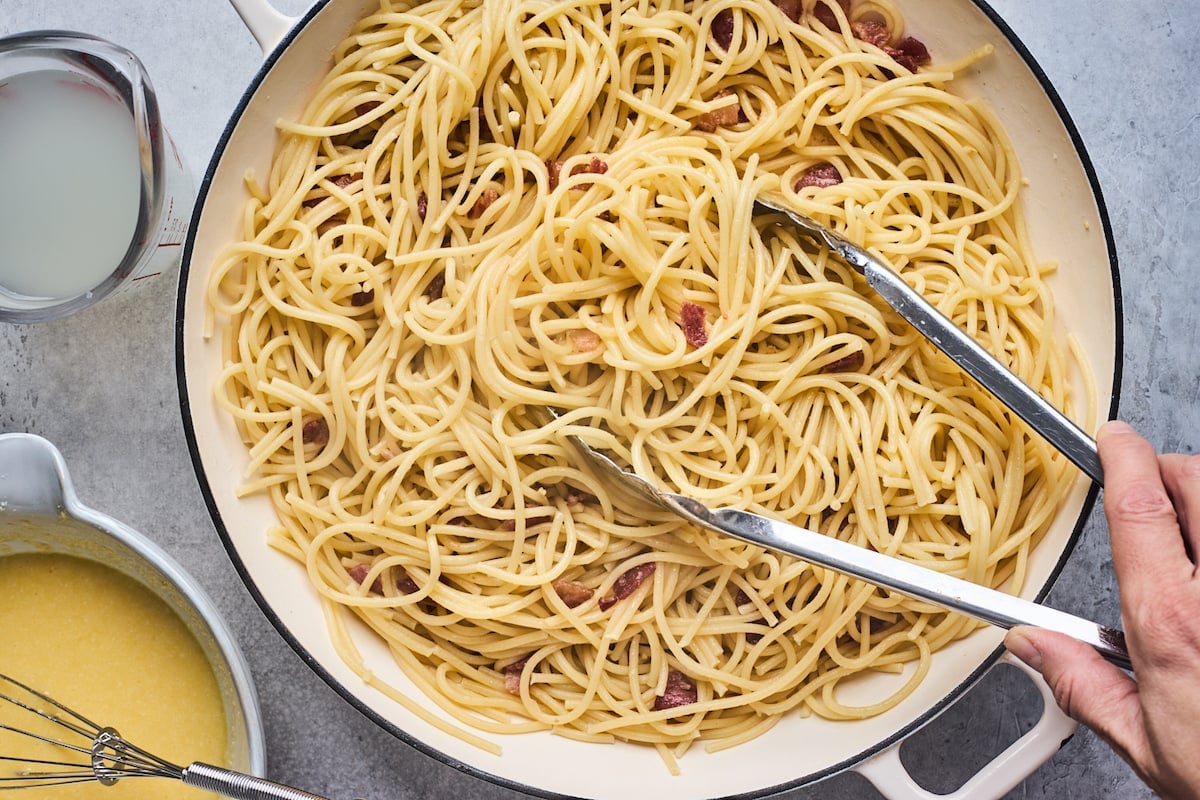 spaghetti carbonara in pot with tongs.