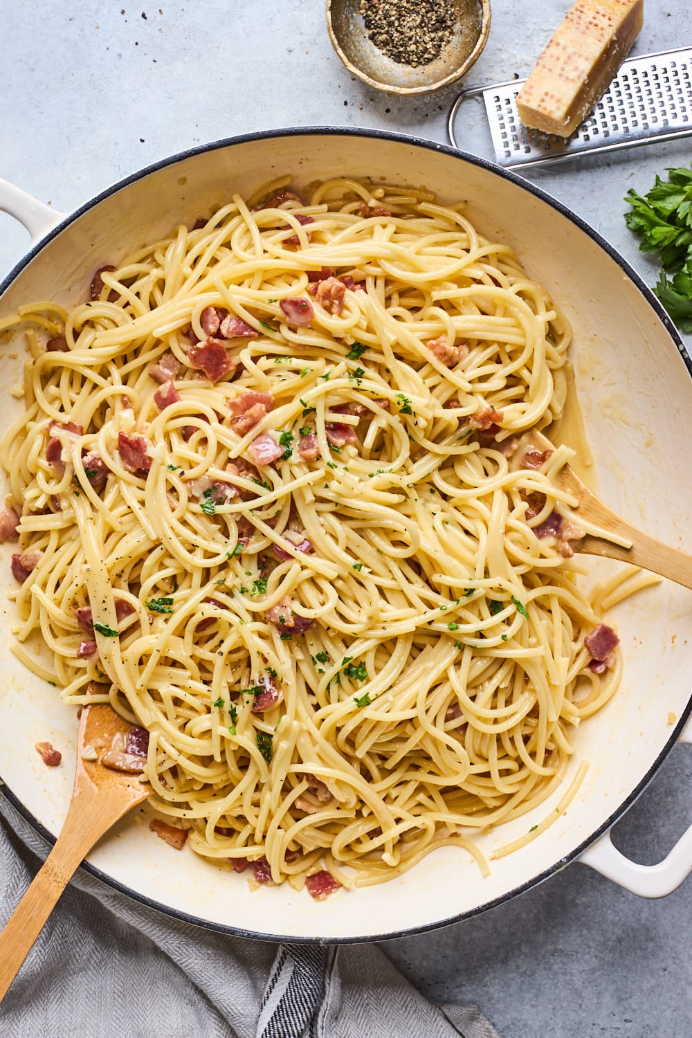 spaghetti carbonara being tossed in pot with wooden spoons.