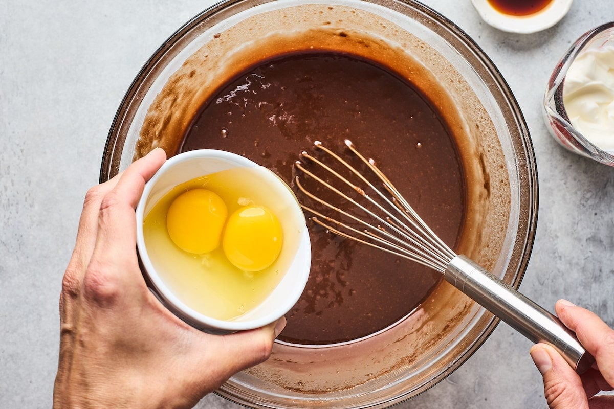 whisking in eggs to chocolate cake batter in large bowl. 