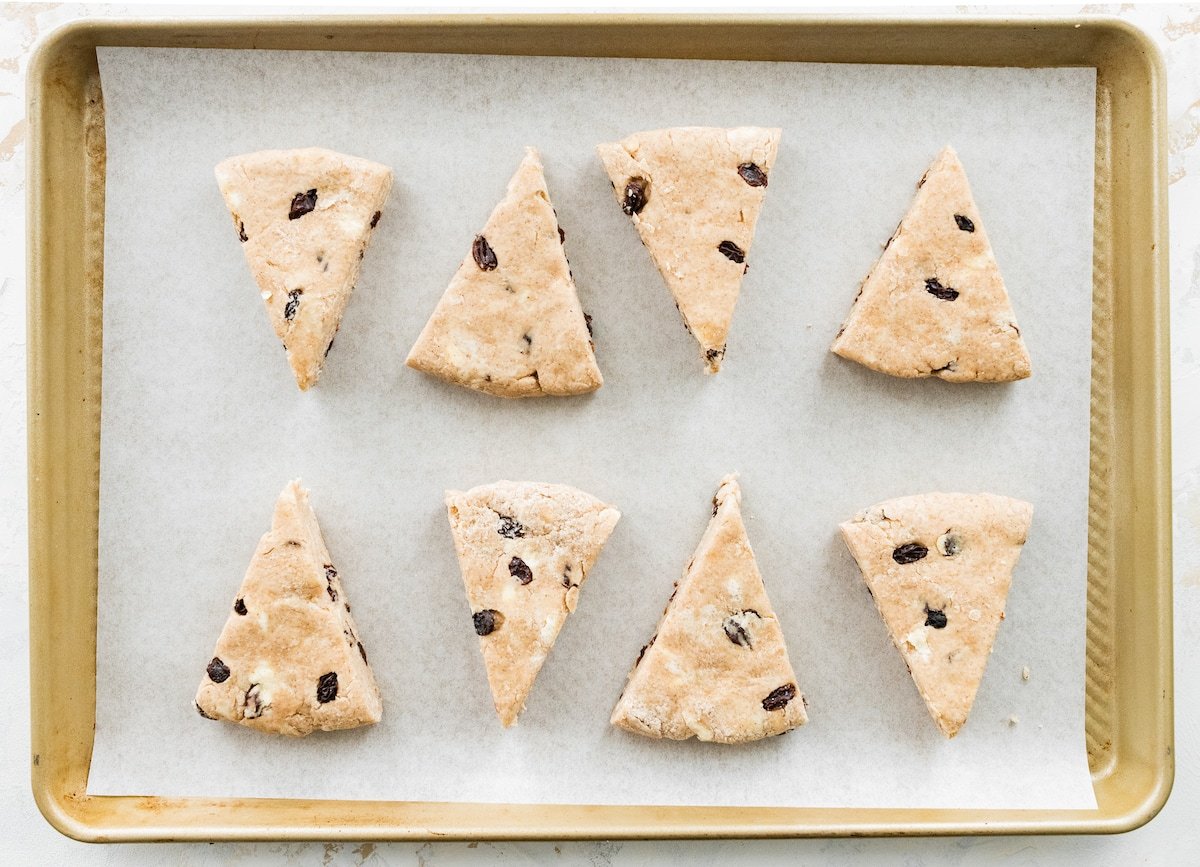 cinnamon raisin scones cut into triangles on large baking sheet with parchment paper. 