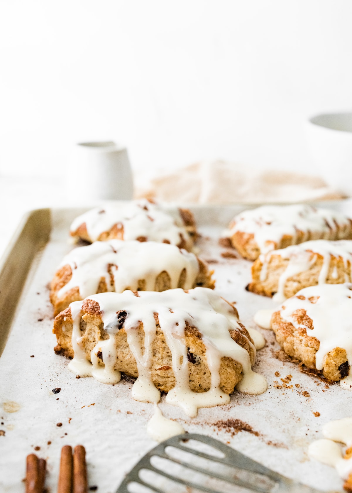 cinnamon raisin scones with drizzle of vanilla glaze on baking sheet with parchment paper. 