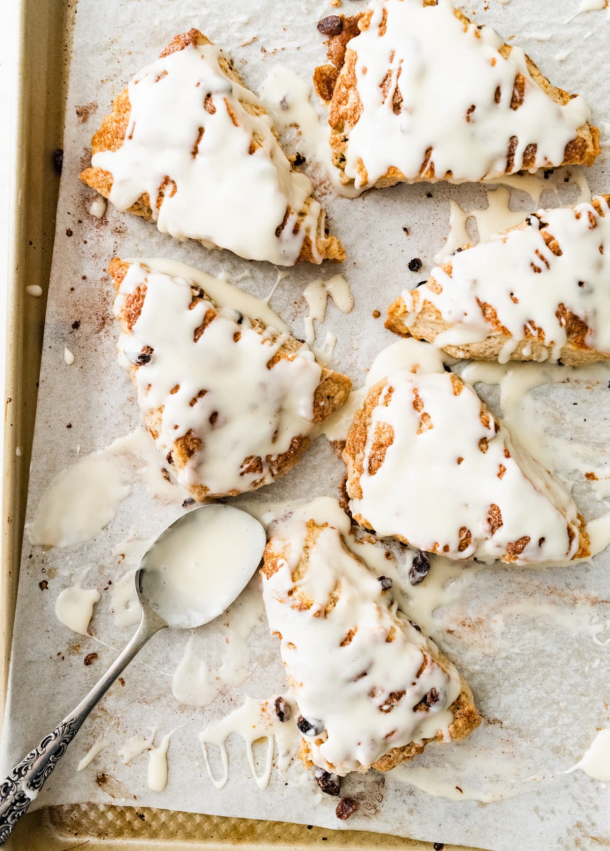 cinnamon raisin scones with vanilla glaze on baking sheet with spoon. 