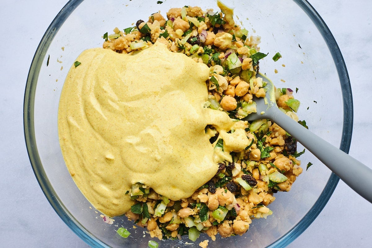 curried chickpea salad in bowl with creamy curry dressing and spatula. 