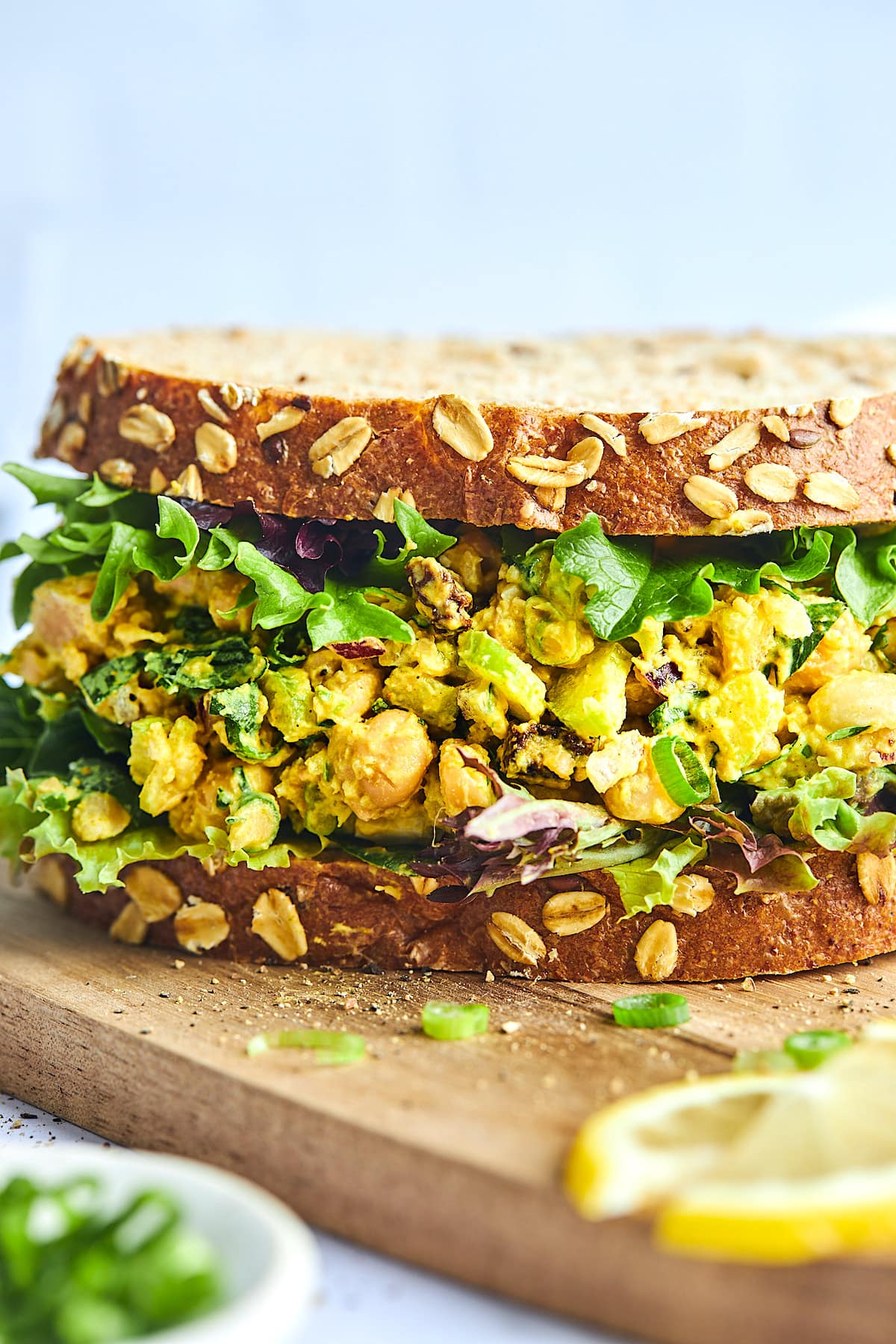 curried chickpea salad in between two slices of whole wheat bread on wood cutting board.