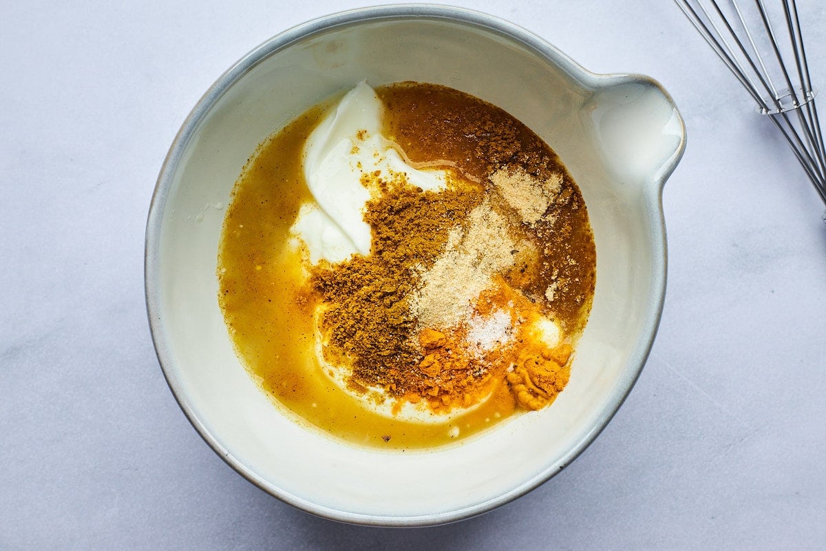 Greek yogurt dressing in bowl with lemon juice, maple syrup, curry powder, turmeric powder, and garlic powder.