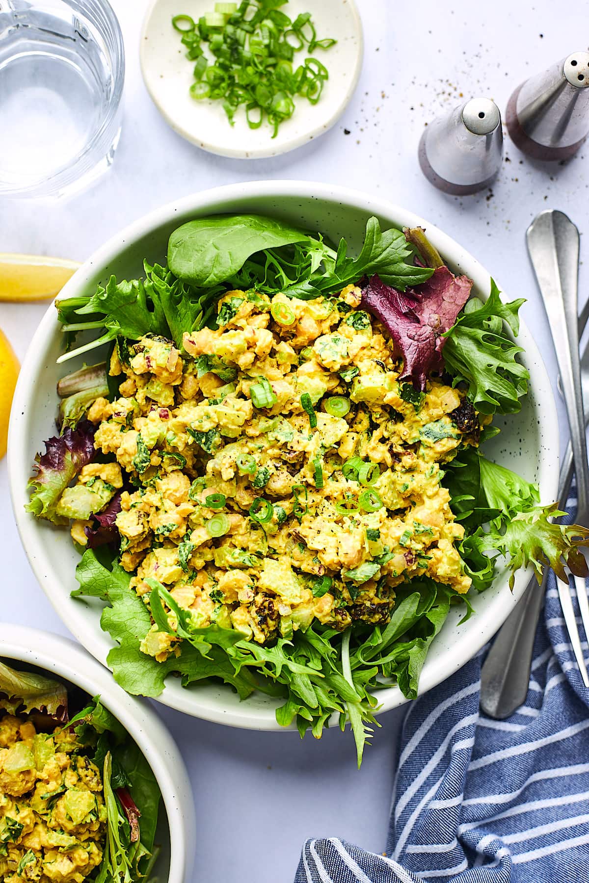 curried chickpea salad on bed of greens in white bowl.
