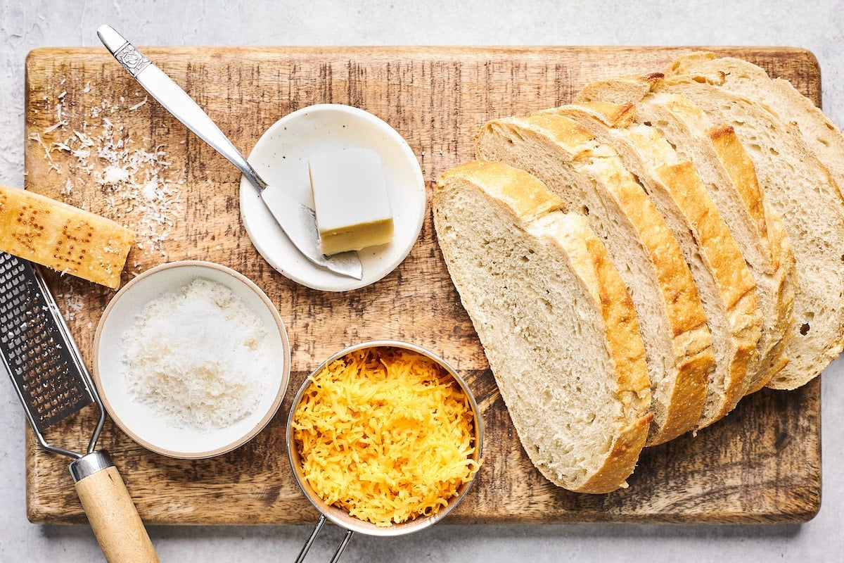 slices of bread, shredded cheese, and butter on wood board to make grilled cheese.