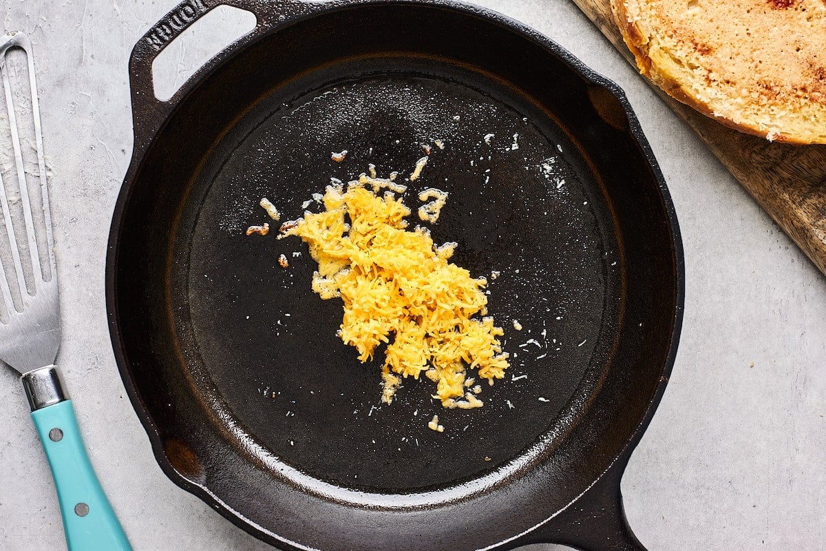 shredded cheddar cheese cooking in cast iron skillet to make cheese crust on grilled cheese. 