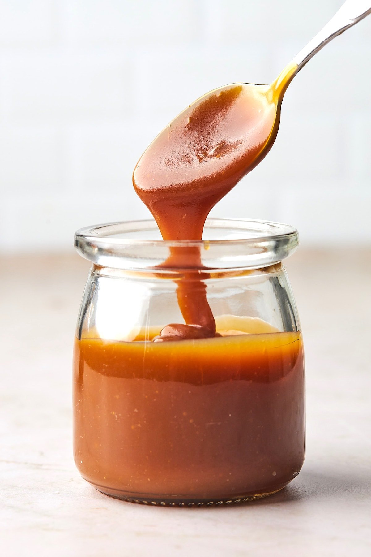 salted caramel sauce on spoon dripping into jar. 