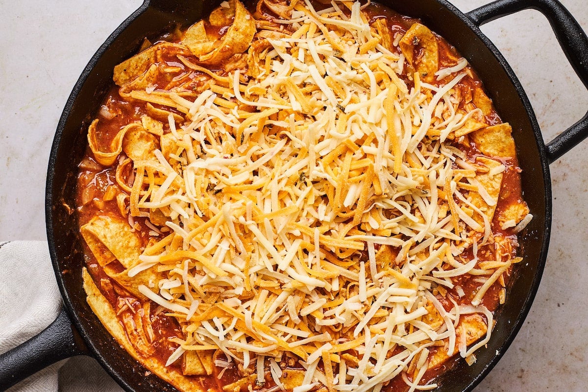 skillet chicken enchiladas topped with shredded cheese in cast iron skillet. 
