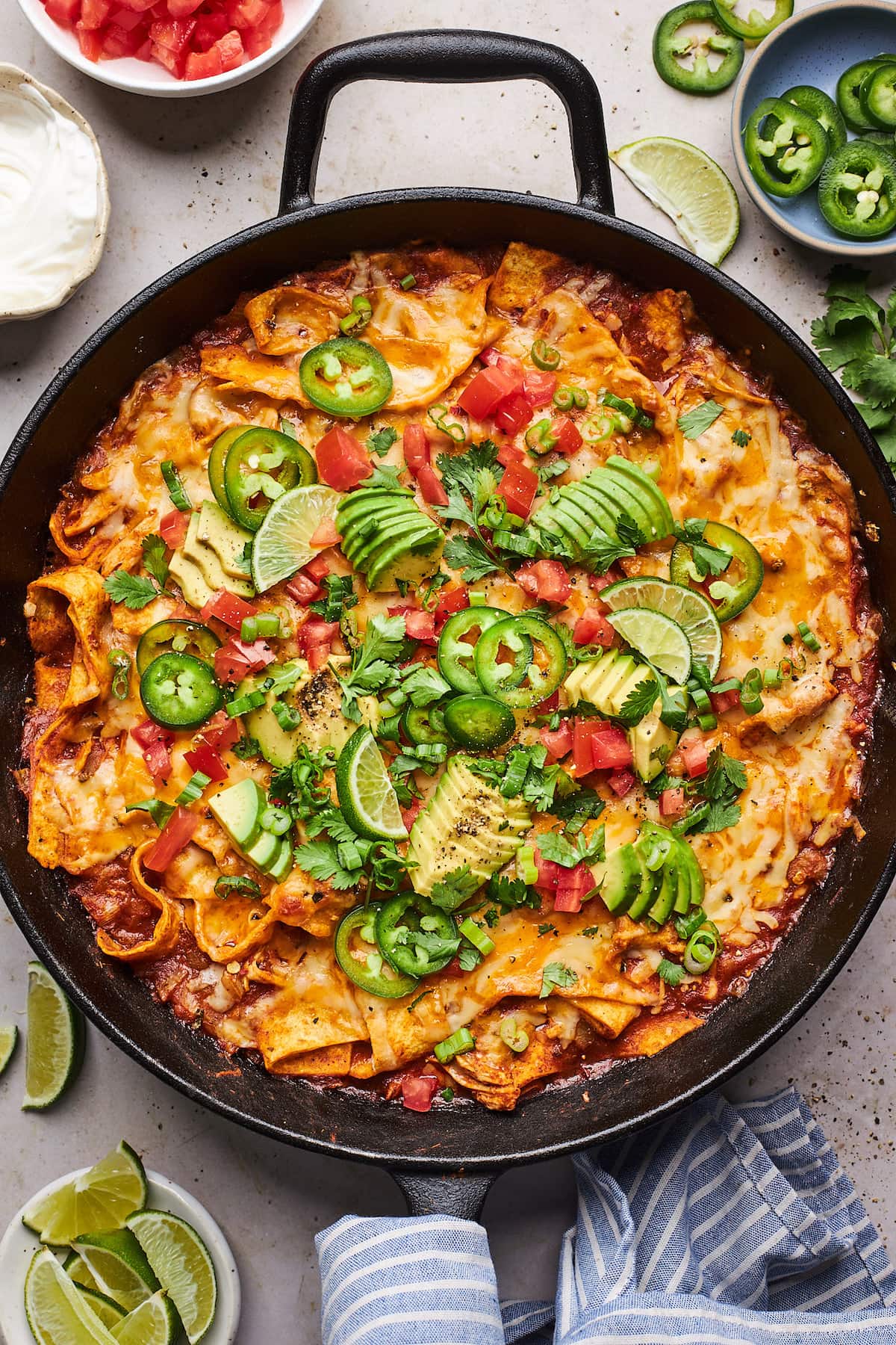 skillet chicken enchiladas in cast iron skillet with avocado, jalapeño slices, lime wedges, and diced tomatoes. 