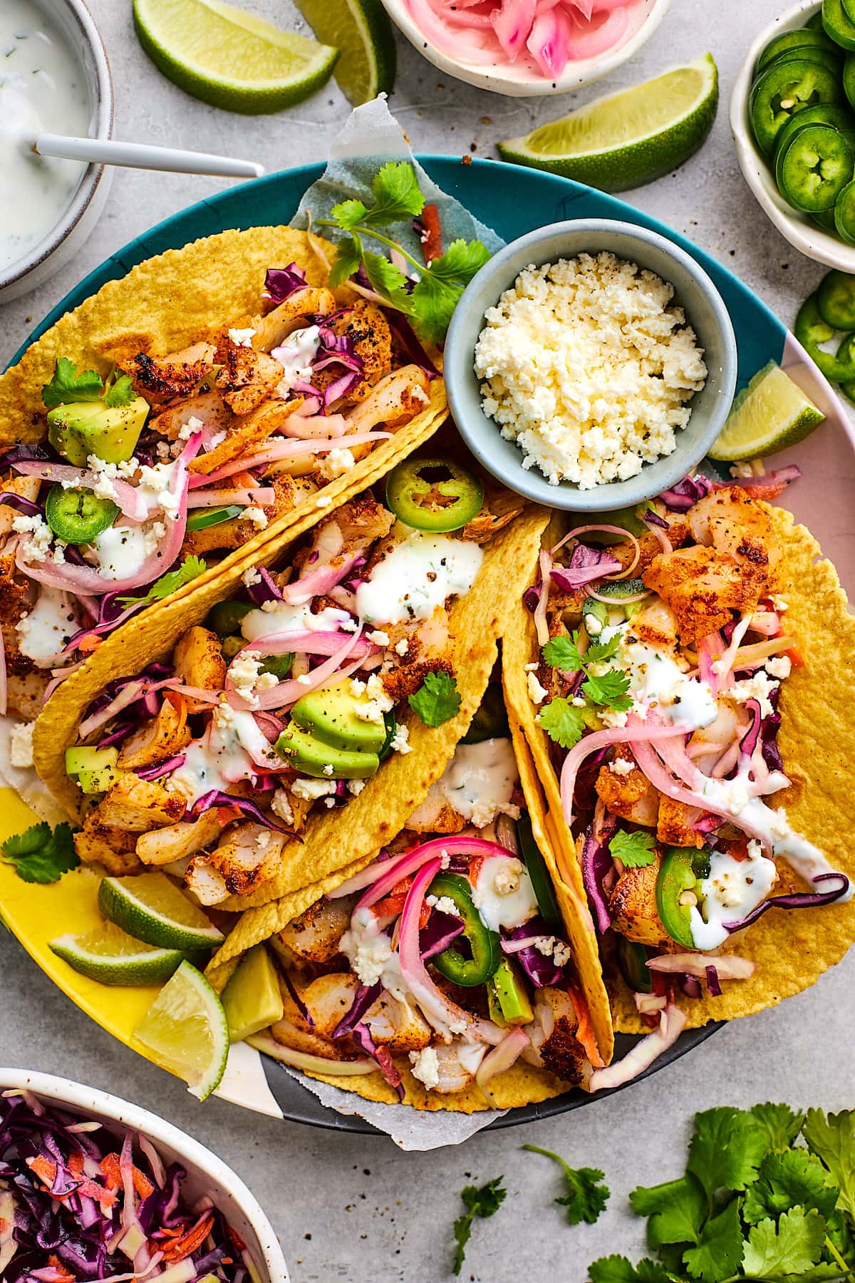 fish tacos on plate with toppings and small bowl of cotija cheese. 