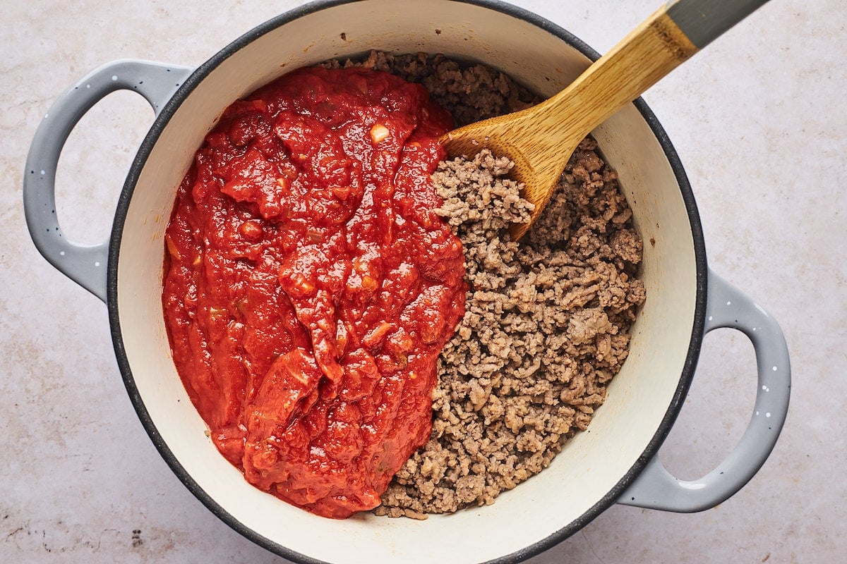lazanya yapmak için tahta kaşıkla büyük tencerede marinara soslu kıyma ve İtalyan sosisi pişirme. 
