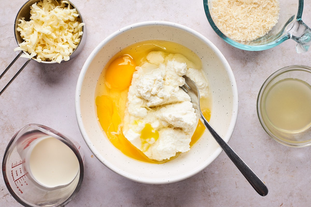lazanya için dolgu yapmak için peynirli kaşıkla bir kasede ricotta peyniri ve yumurta. 