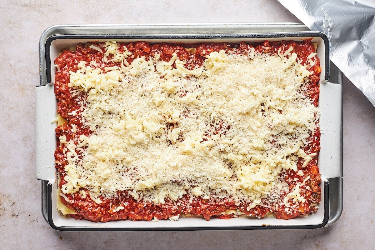 layering lasagna in pan with meat sauce, noodles, and cheese. 