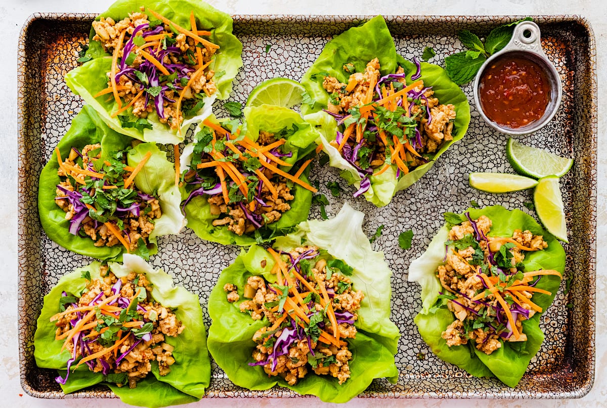 chicken lettuce wraps on serving tray with chili sauce and lime wedges. 