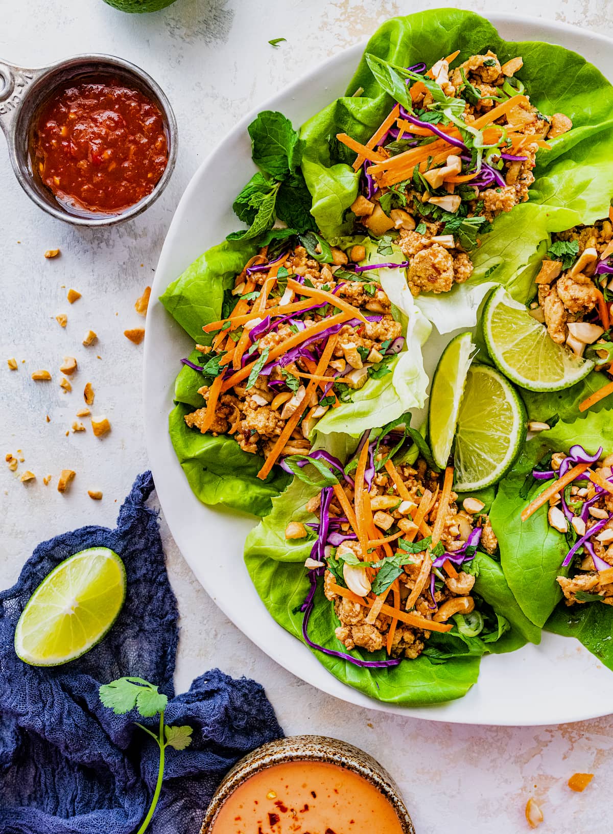 Lettuce wraps with ground chicken, veggies, cashews, and lime wedges on plate with chili sauce on the side. 