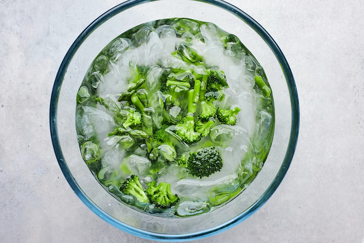 cooked broccoli and asparagus in bowl of ice water. 