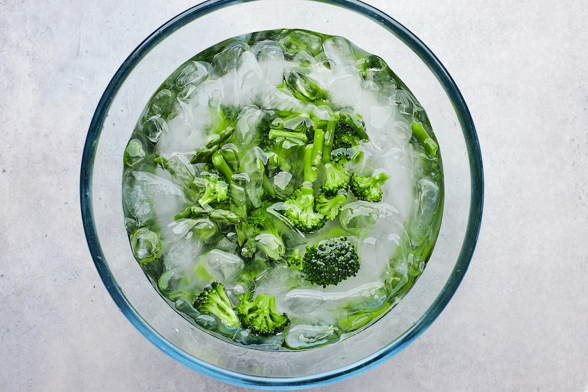 cooked broccoli and asparagus in bowl of ice water.