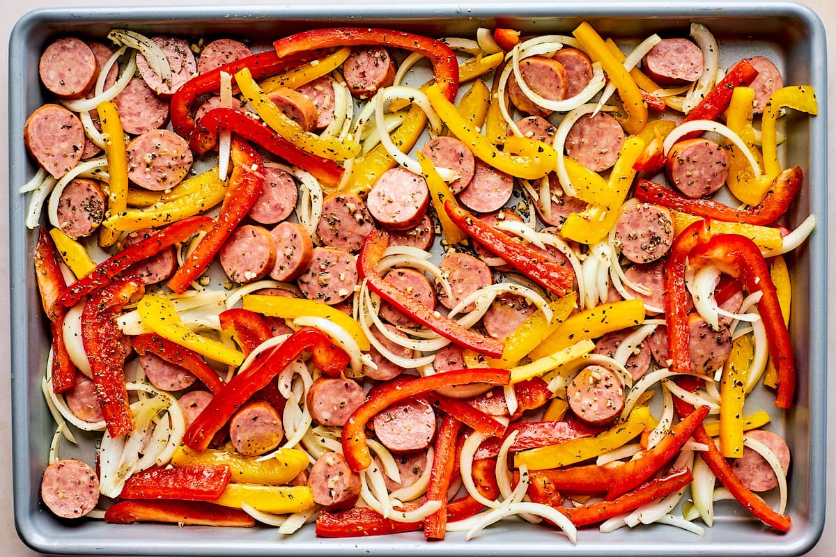 sliced sausage rounds, bell pepper strips, and onion, on large sheet pan with spices. 