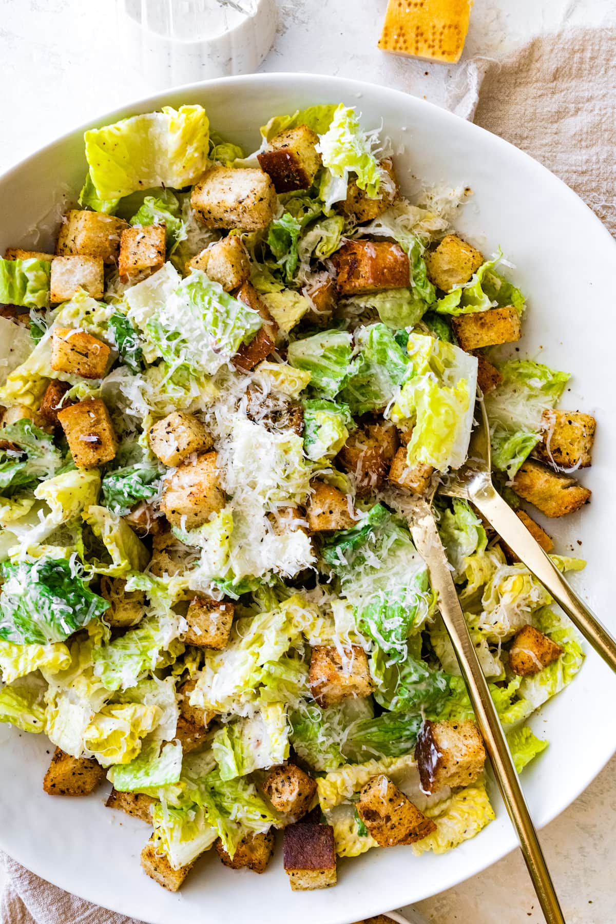 Caesar salad in white bowl with gold salad servers. 