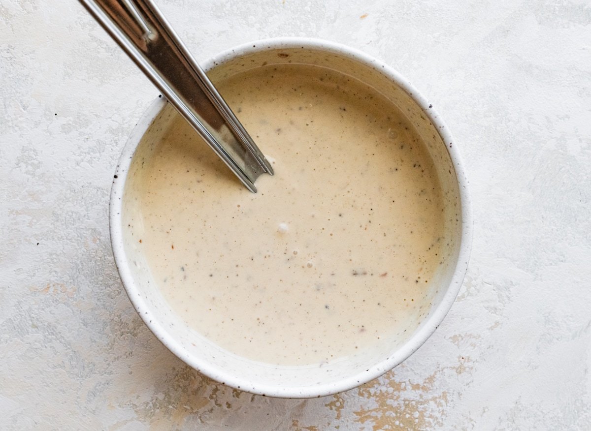caesar dressing in bowl with whisk. 
