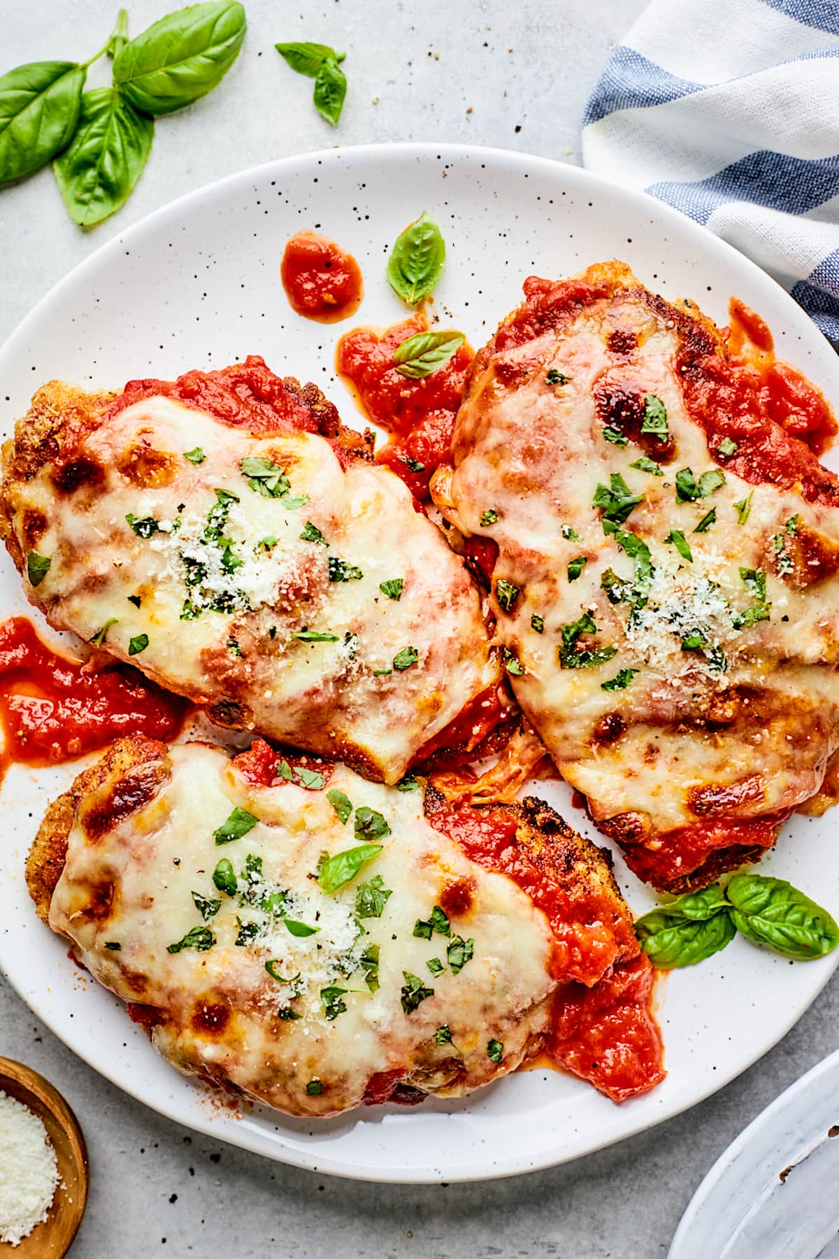 3 chicken parmesan pieces on plate with marinara sauce, melted mozzarella cheese, and fresh basil. 