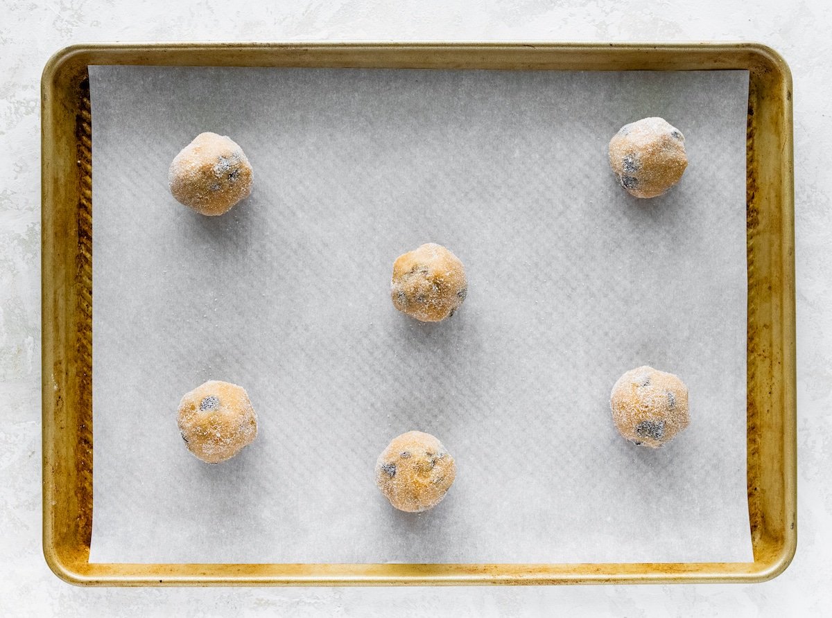 peanut butter chocolate chip cookie dough balls rolled in sugar and placed on baking sheet with parchment paper. 