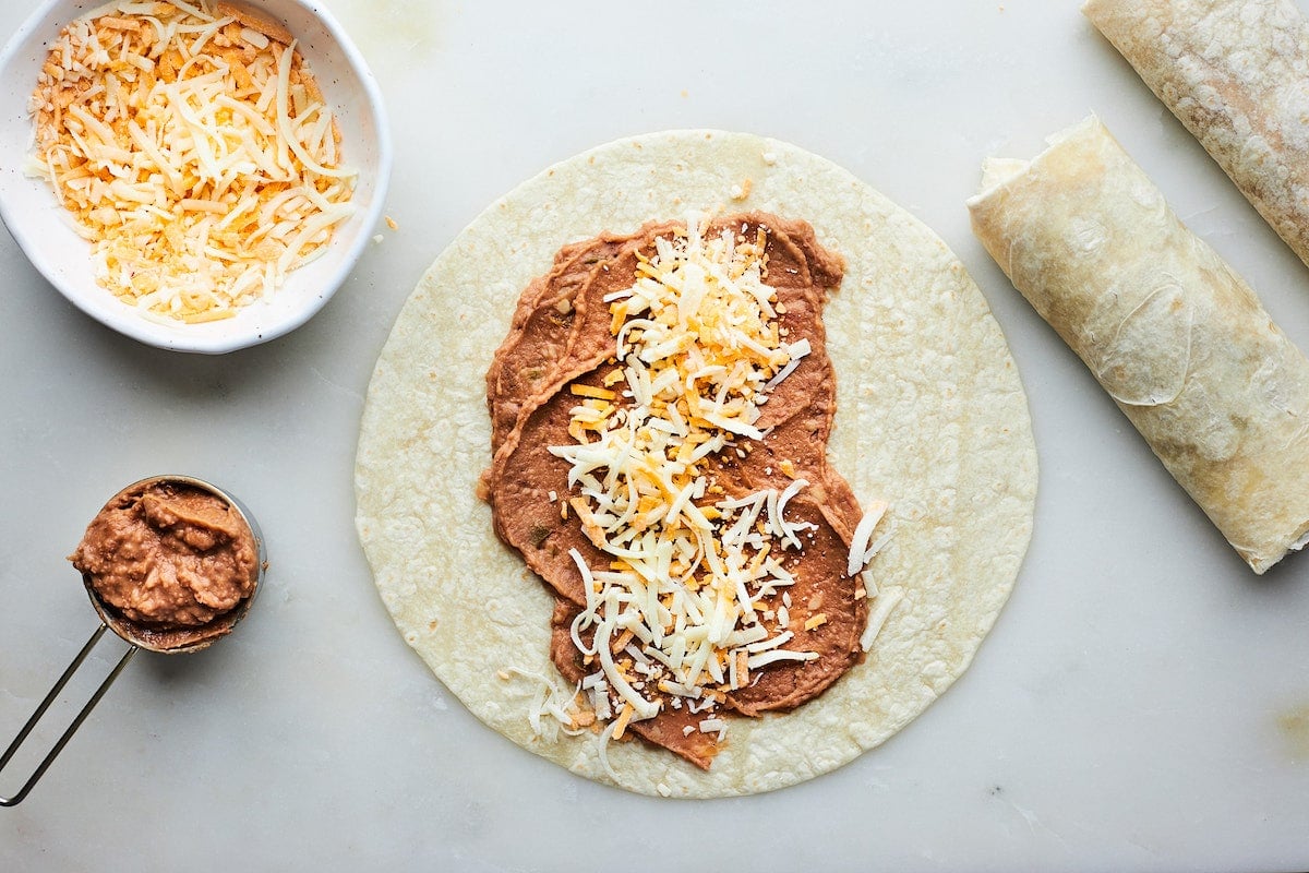 making a bean and cheese burrito with a flour tortilla, refried beans and shredded cheese.