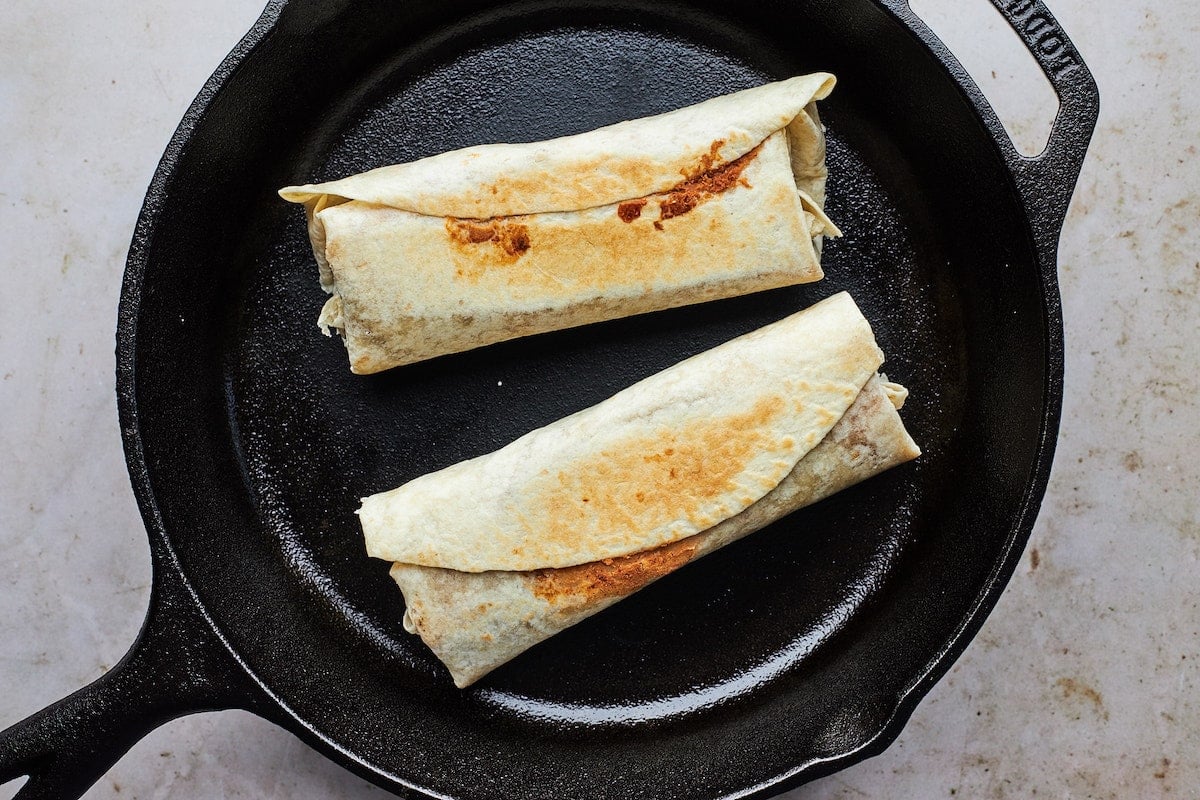 two bean and cheese burritos in cast iron skillet. 