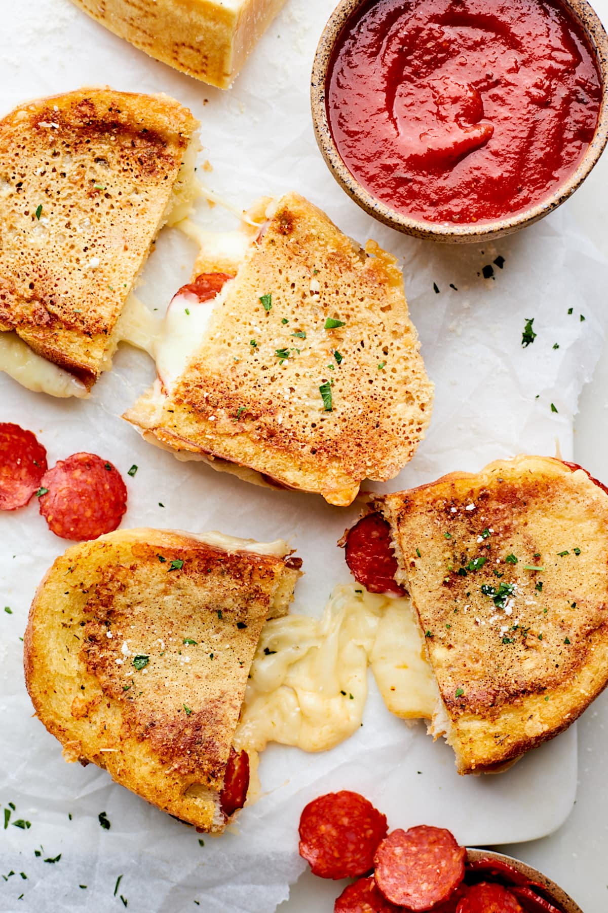 pepperoni grilled cheese sandwiches cut in half with melty cheese and a bowl of pizza sauce for dipping.