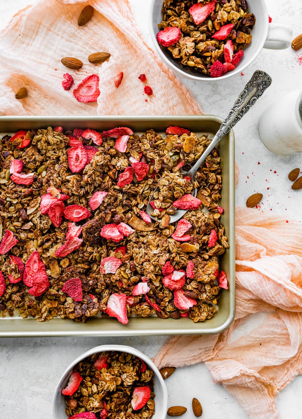 strawberry granola on baking sheet with large spoon. 