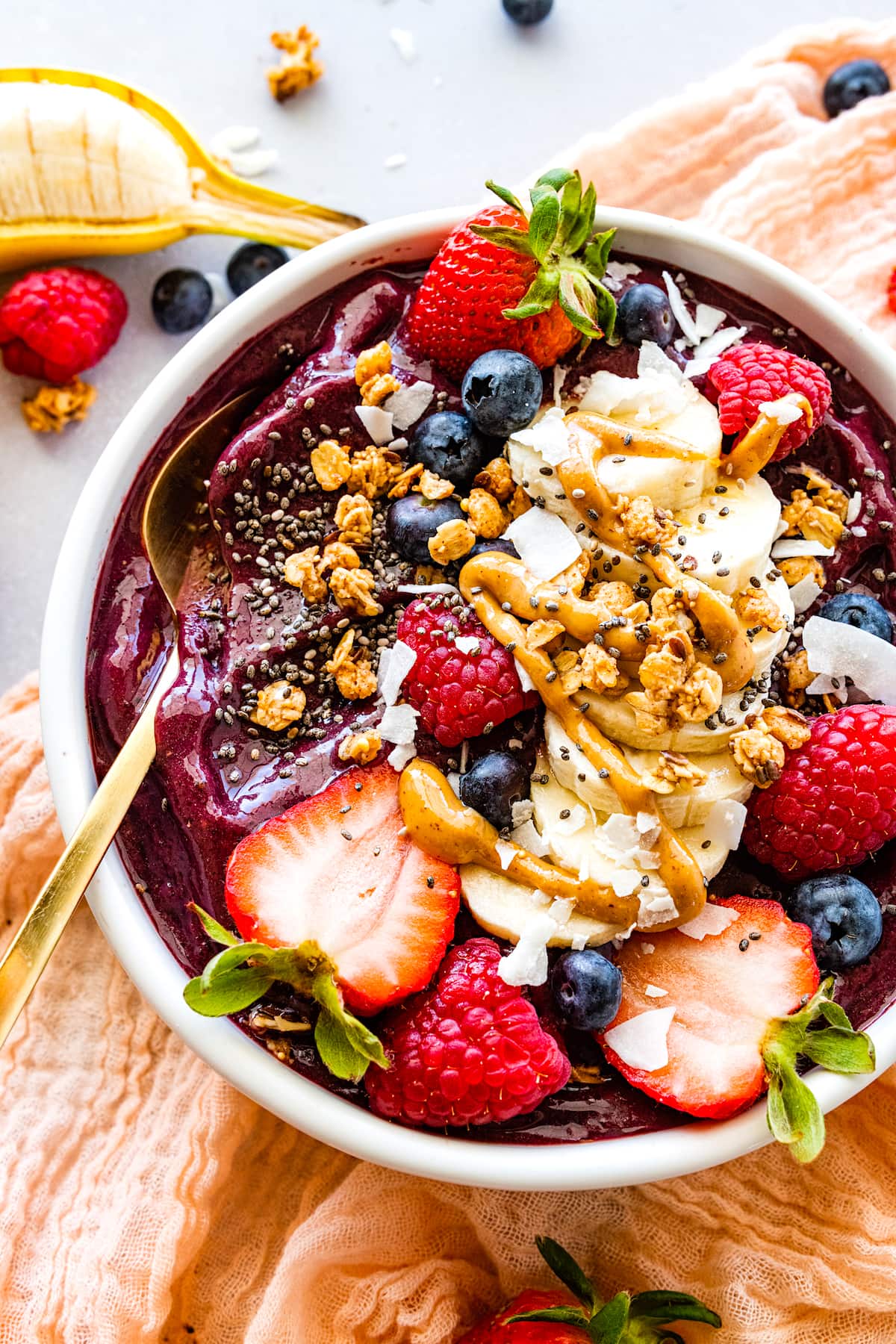 acai bowl with fresh fruit, chia seedds, coconut, drizzle of nut butter, and gold spoon. 