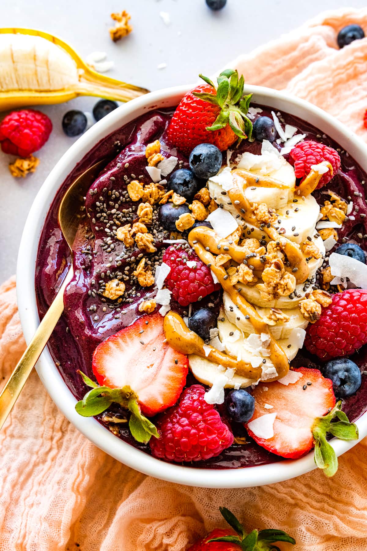 acai bowl with fresh fruit, chia seedds, coconut, drizzle of nut butter, and gold spoon.