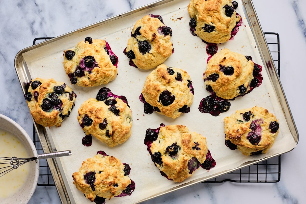 blueberry biscuits on baking sheet with parchment paper on cooling rack. 