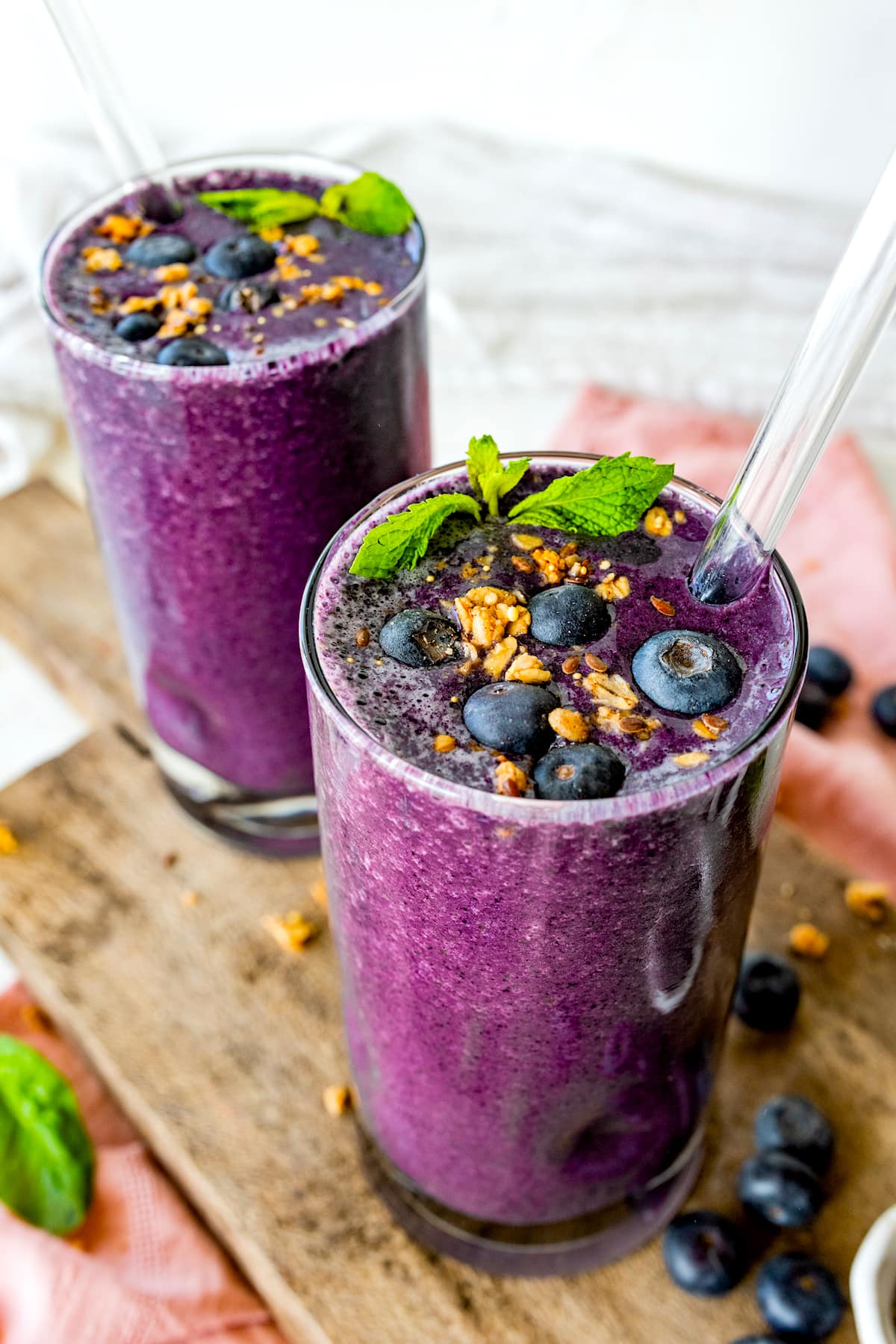 2 blueberry smoothies with glass straws with granola on top, fresh mint, and fresh blueberries. 