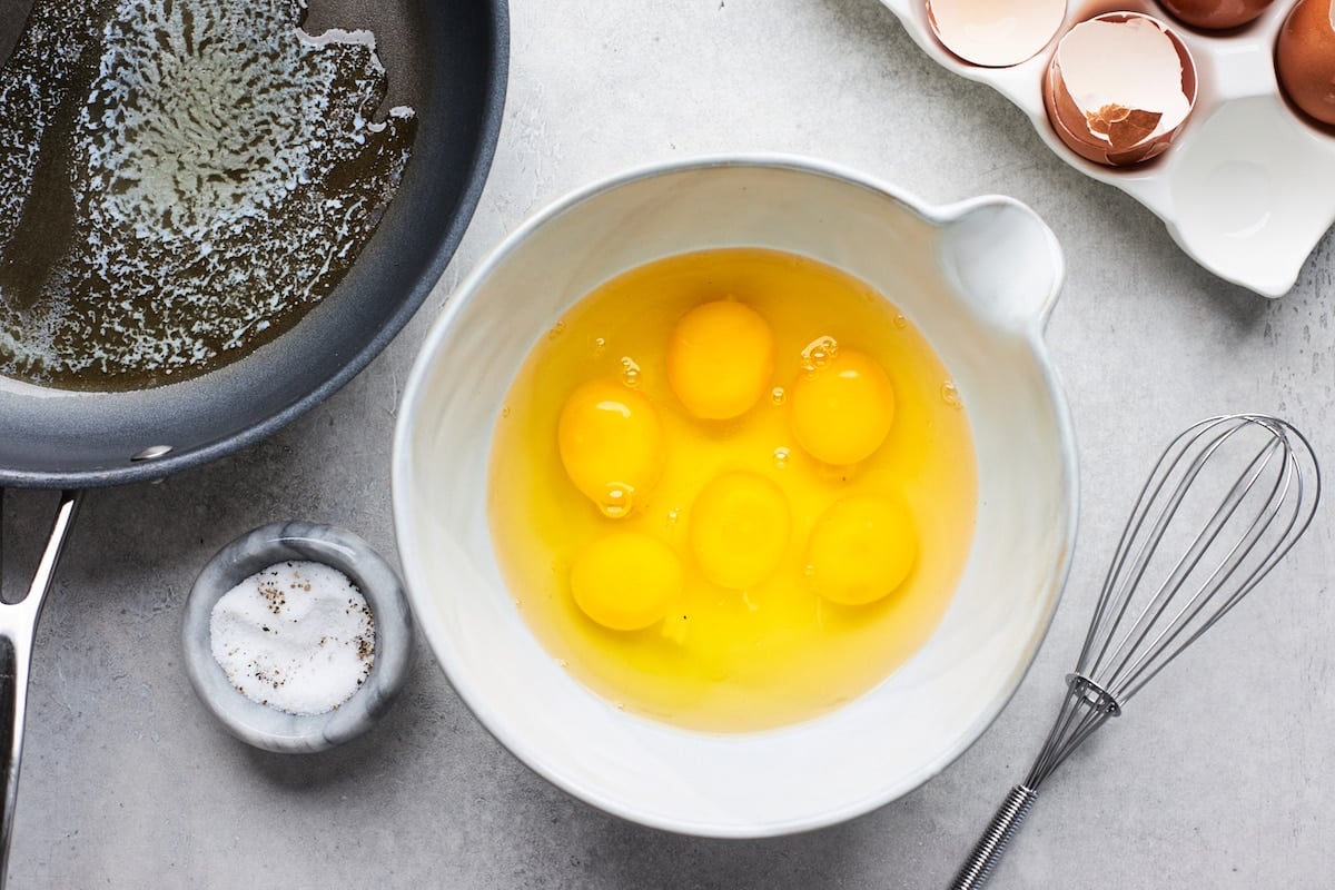 eggs in mixing bowl with whisk and skillet. 