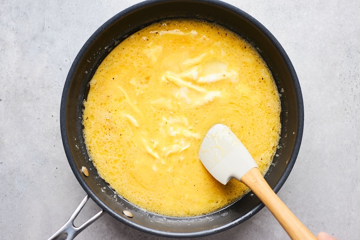 scrambled eggs cooking in skillet with spatula. 
