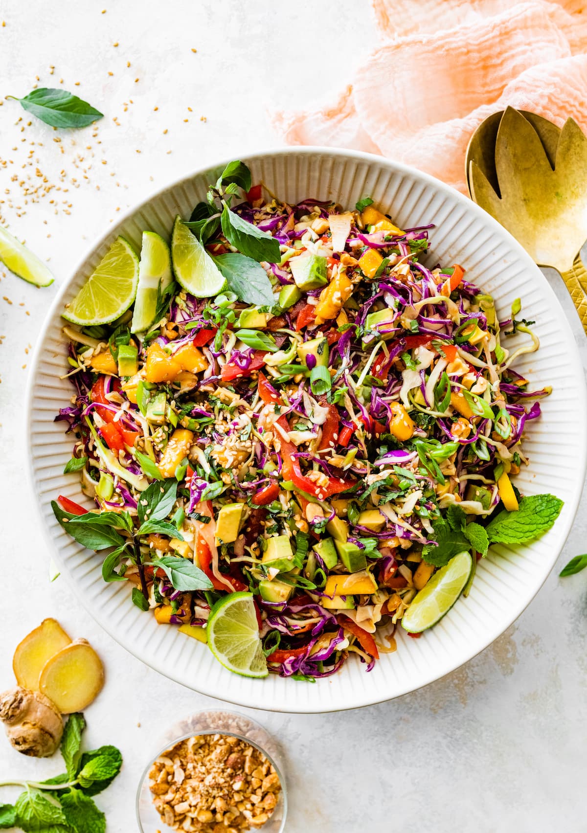Cabbage salad with mango, avocado, fresh herbs, sesame seeds, and lime wedges in serving bowl. 