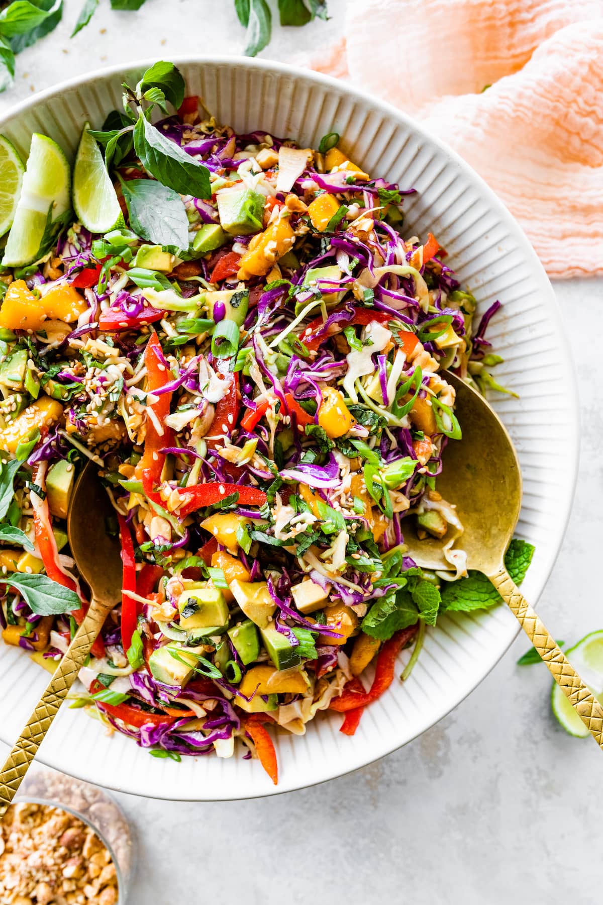 colorful cabbage salad with mango, avocado, and sesame seeds in serving bowl with serving spoons. 