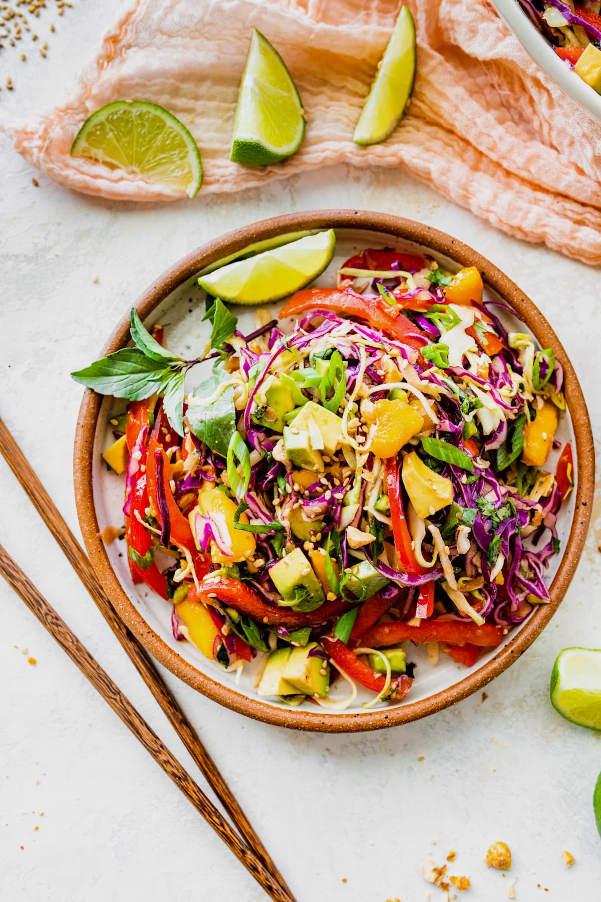 cabbage salad in bowl with chopsticks and lime wedges. 