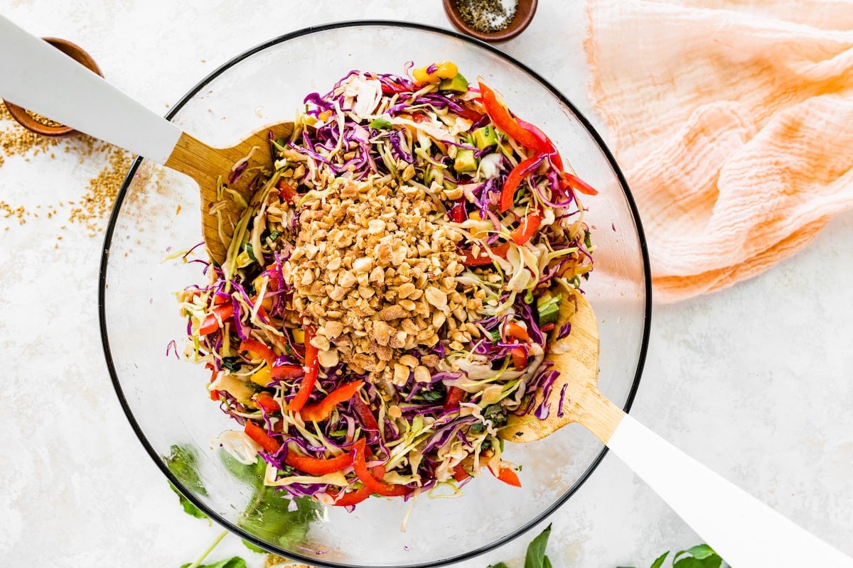 cabbage salad topped with chopped peanuts in serving bowl with tongs. 